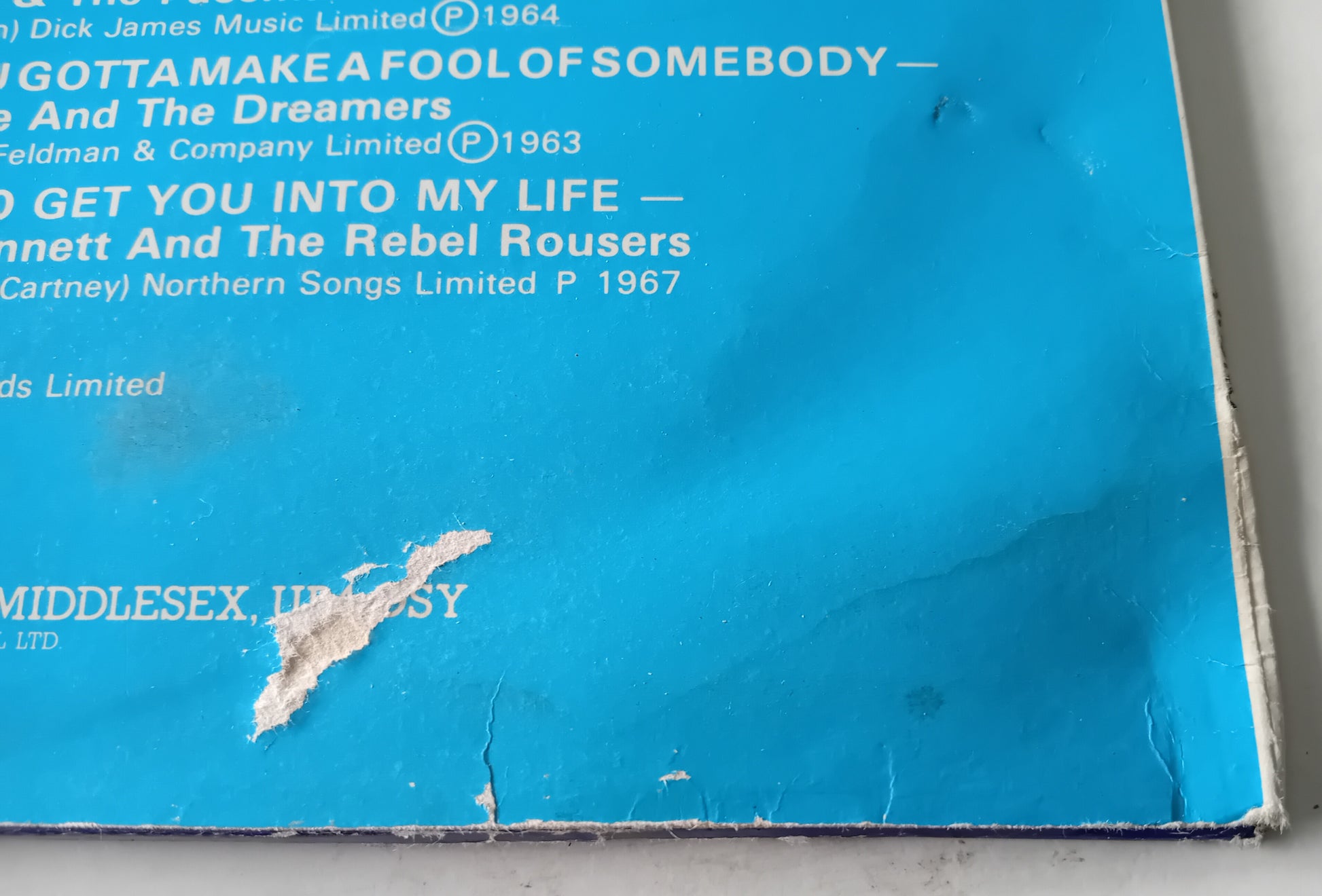 Close-up of a blue record sleeve with text and a tear on the corner.