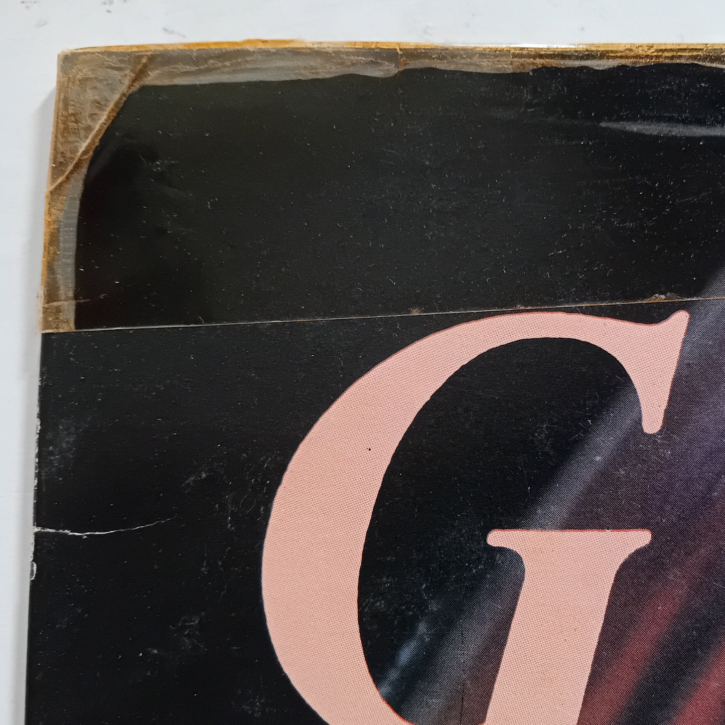 Close-up of a vinyl record with a large pink letter 'G' on a black background.