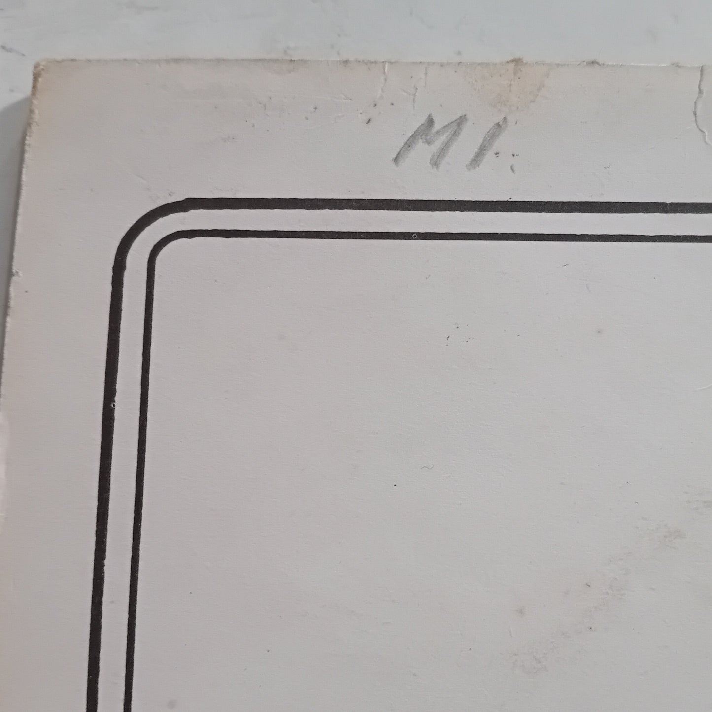 Corner of a white card with black border and 'MI' initials on a light gray background
