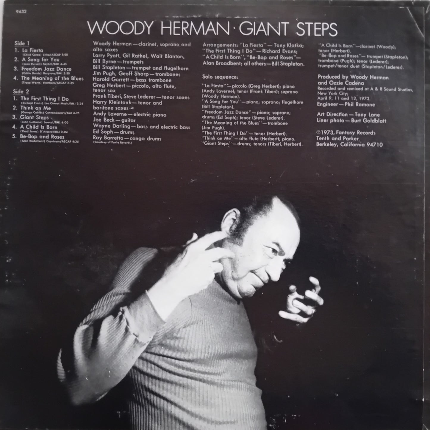 The back cover of a Woody Herman 'Giant Steps' vinyl record album, featuring a black background with white text listing track titles and credits, alongside a black-and-white photo of Woody Herman performing on stage.