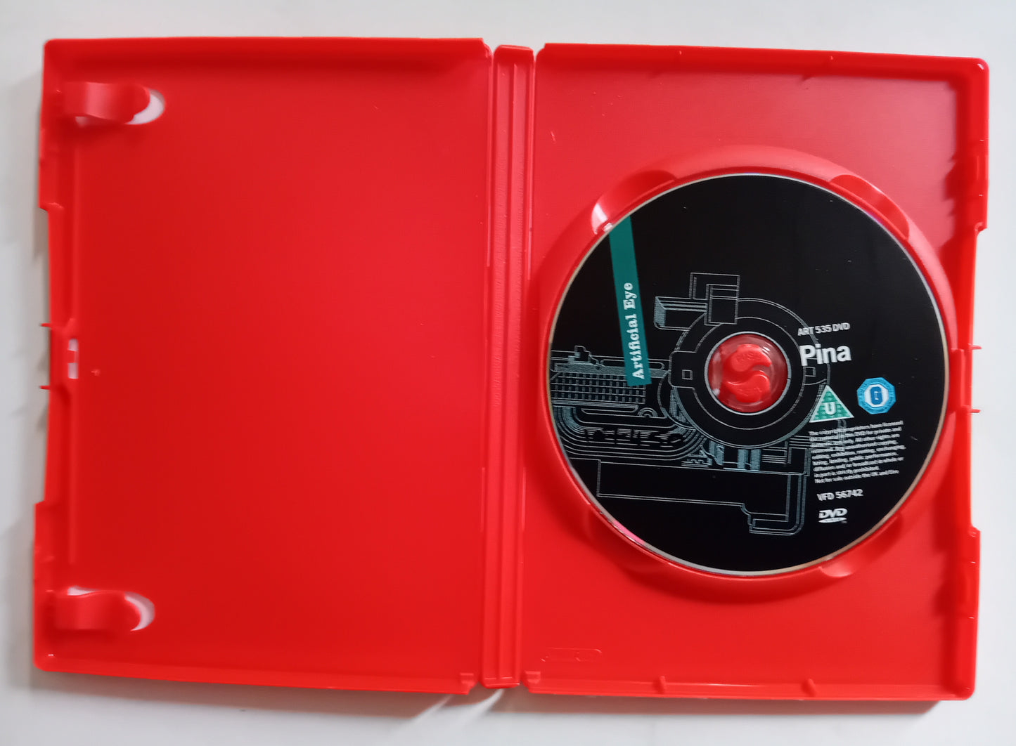 A red plastic DVD case opened flat, with a black DVD disc inserted on the right side. The disc features a technical schematic design with the text 'Pina' and 'DVD VIDEO' visible.