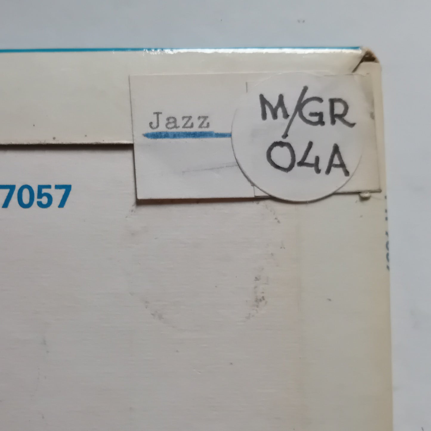 A close-up of a cream-colored paperboard package corner with a white label reading 'Jazz' and a circular handwritten sticker reading 'M/GR 04A'.
