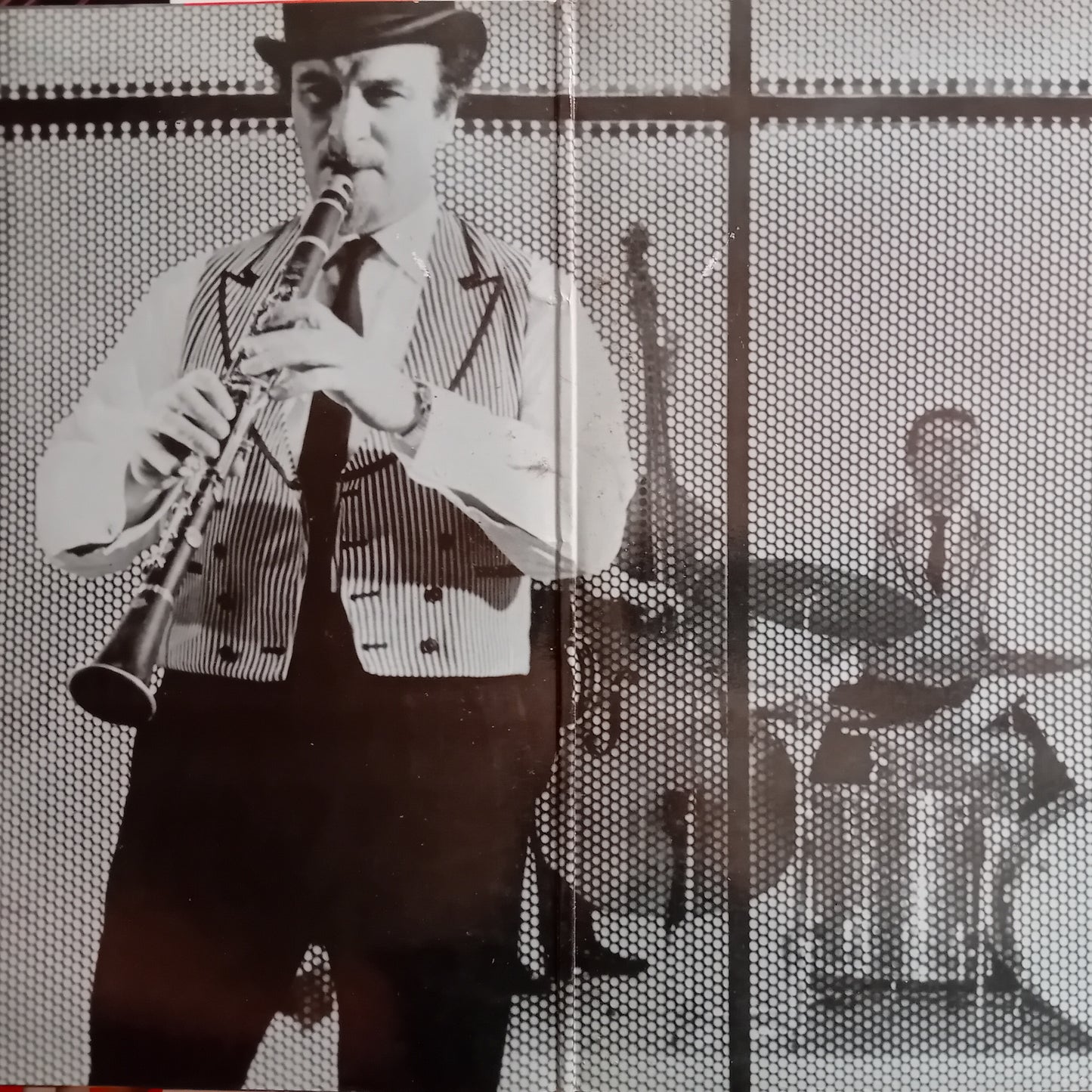 Black and white photo of a man playing a clarinet with musical instruments in the background.