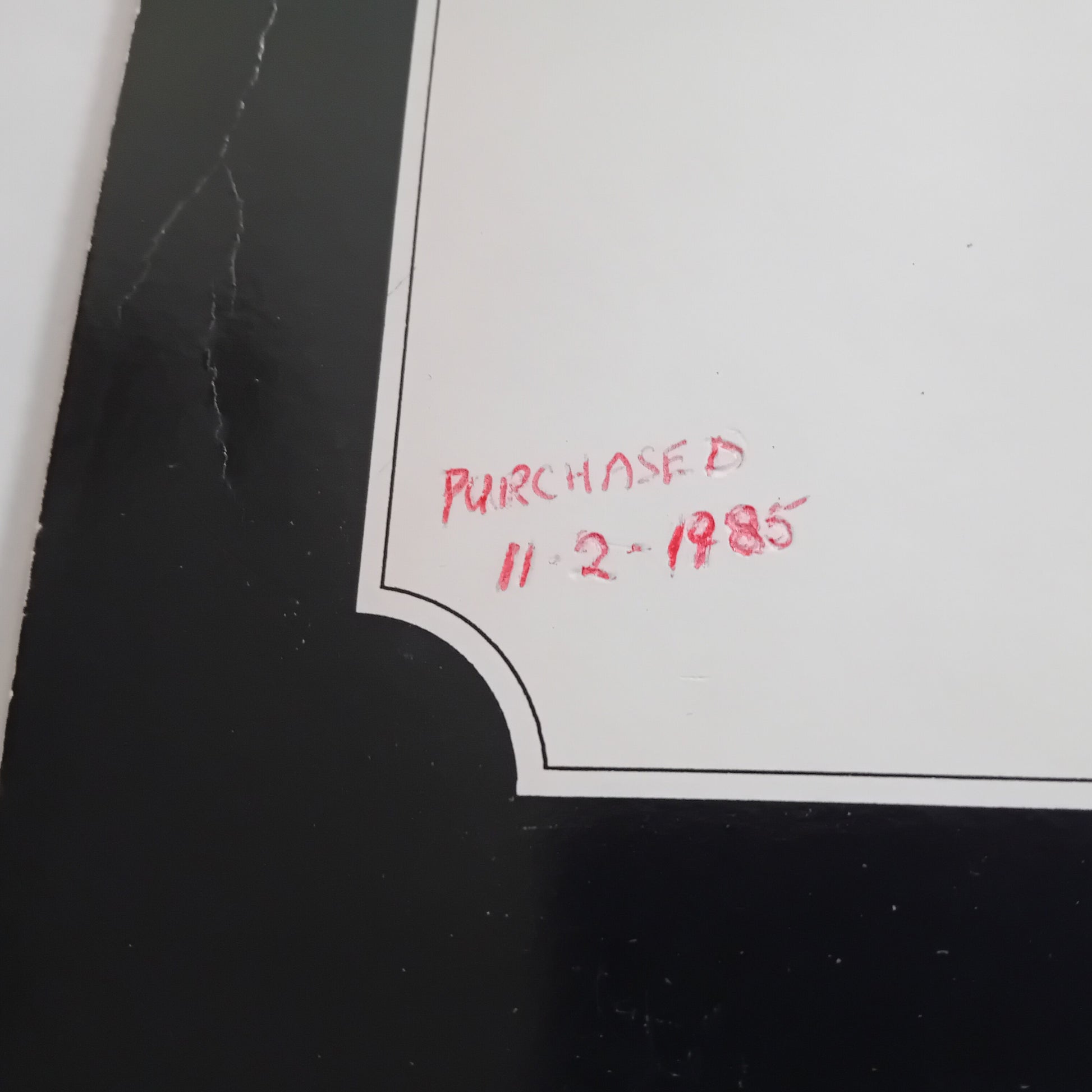 Red text 'PURCHASED 11-2-1985' on a white corner of a black surface.