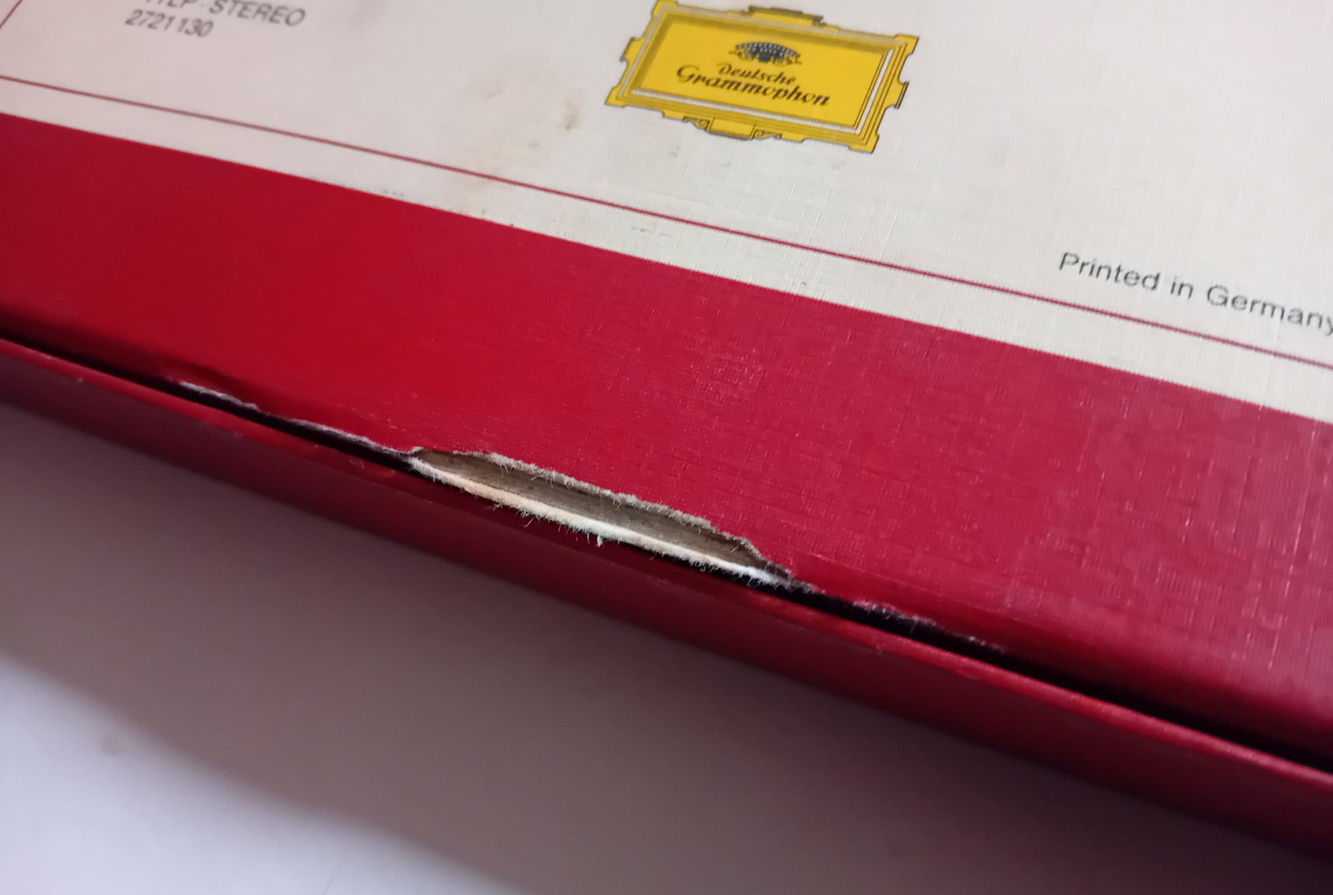 Close-up of a red and white box with a visible tear along the edge, showing part of a yellow Deutsche Grammophon label.