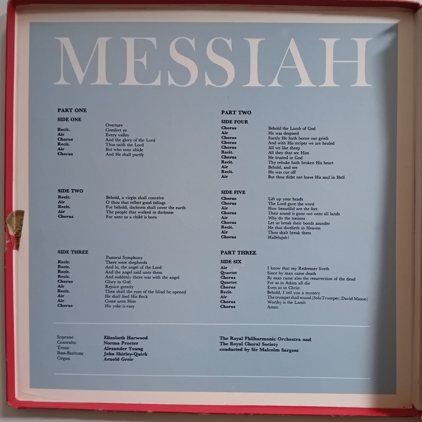 A sheet of printed sheet music titled 'MESSIAH' with multiple parts and song lyrics laid out in columns, photographed inside a red frame or case.