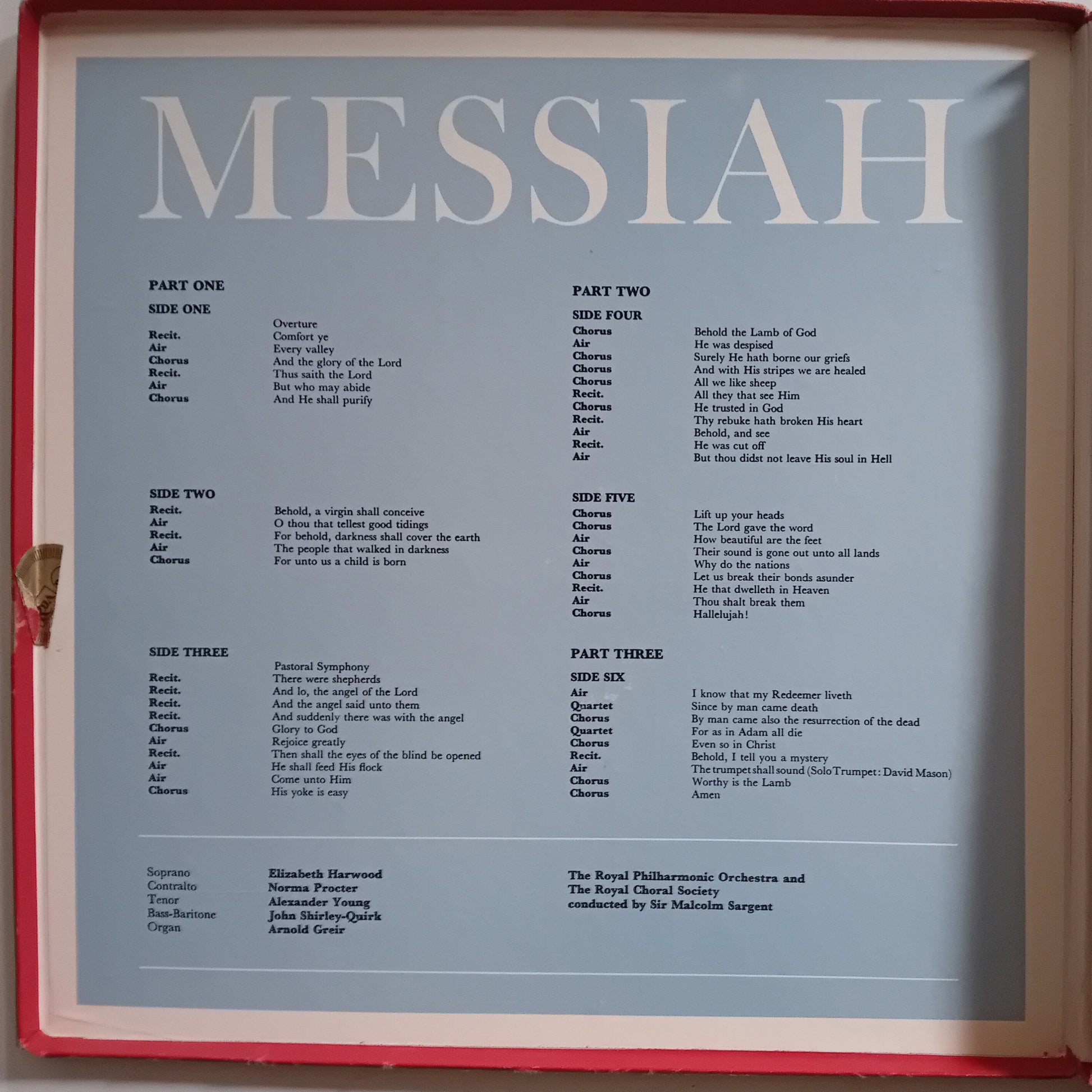 A sheet of printed sheet music titled 'MESSIAH' with multiple parts and song lyrics laid out in columns, photographed inside a red frame or case.