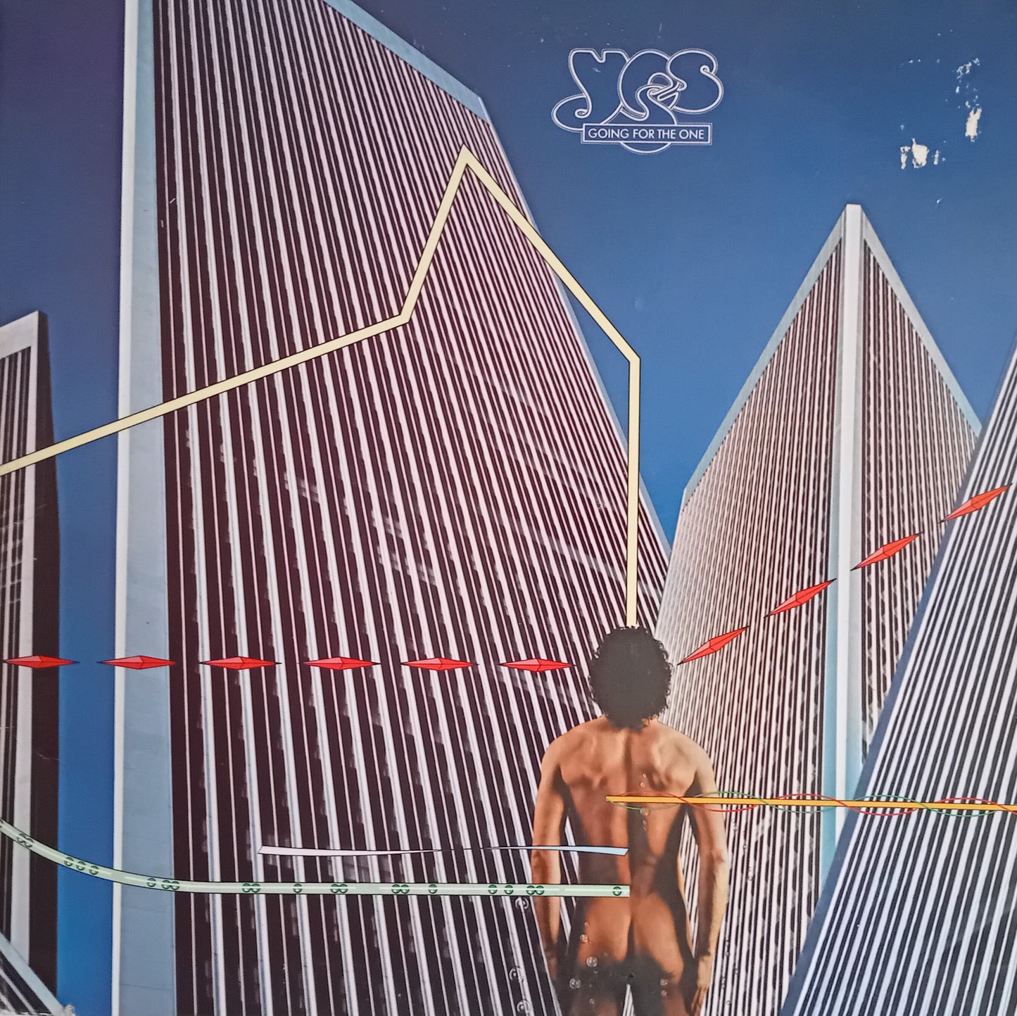 Album cover art for Yes's 'Going For The One' featuring a stylized illustration of a nude male figure from behind, set against towering striped skyscrapers under a blue sky, with the band's logo at the top.