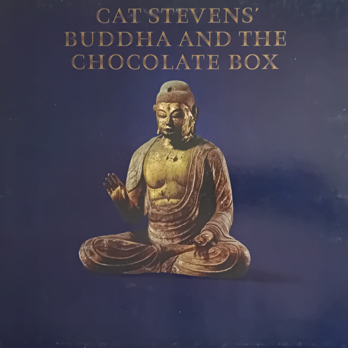 Album cover for Cat Stevens' 'Buddha and the Chocolate Box', featuring a seated Buddha statue against a dark blue background with gold text.