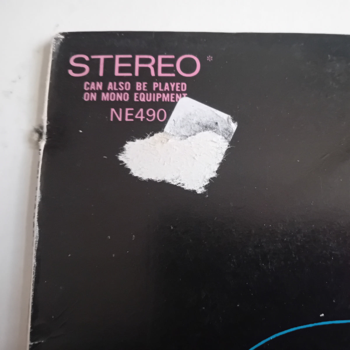 A close-up of a black LP cover corner with pink text reading 'STEREO' and smaller text below, plus a white sticker and surface tear.