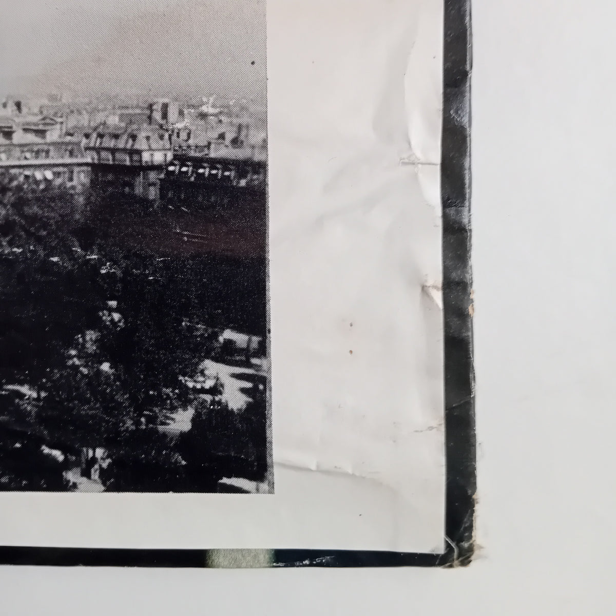 A close-up of a black-and-white printed LP sleeve corner showing a cityscape and trees, with torn or creased white paper edges and dark tape along the border.