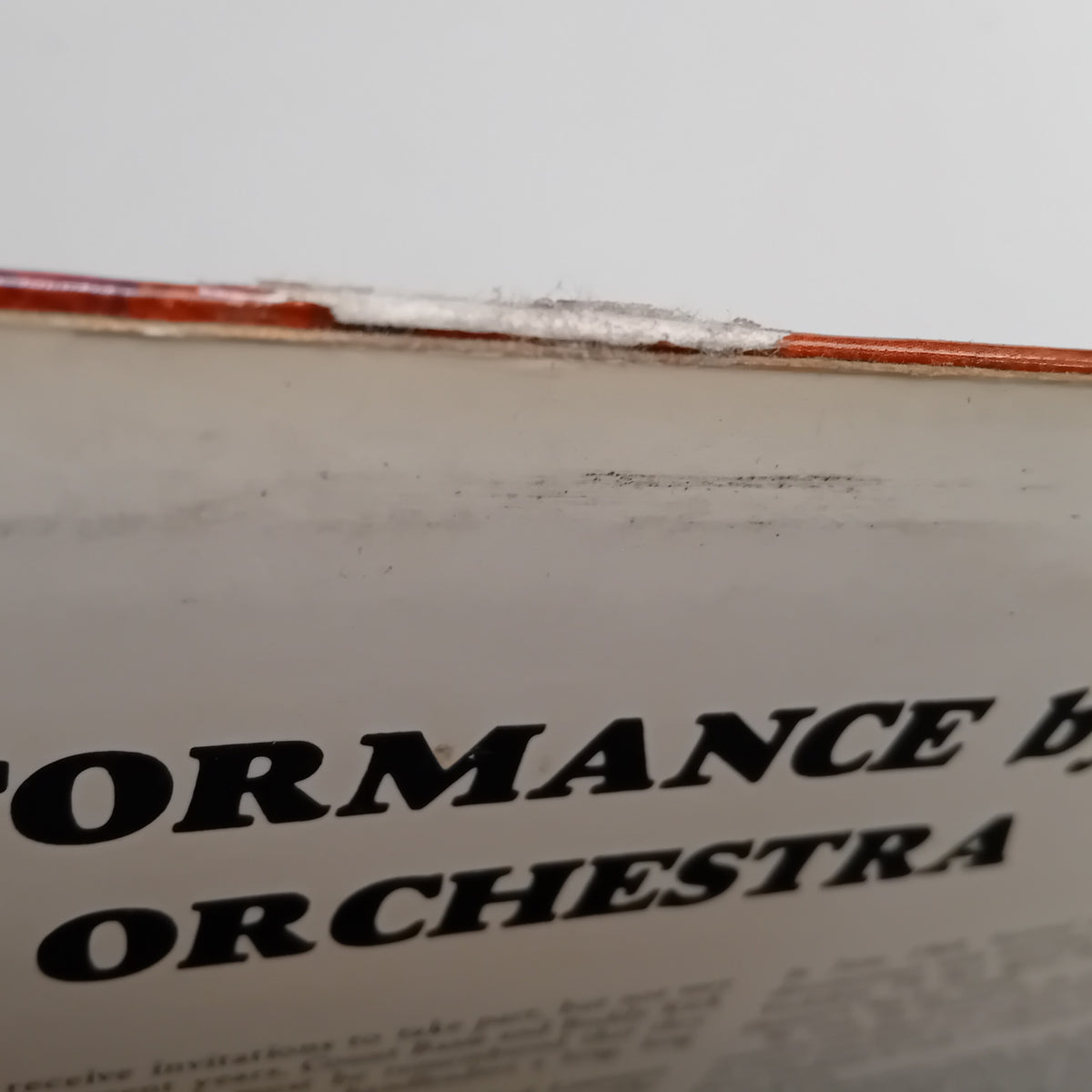 A close-up shot of a vintage printed LP cover with bold black text reading 'PERFORMANCE BY ORCHESTRA' on an off-white background, showing some wear and a red-orange edge along the top.