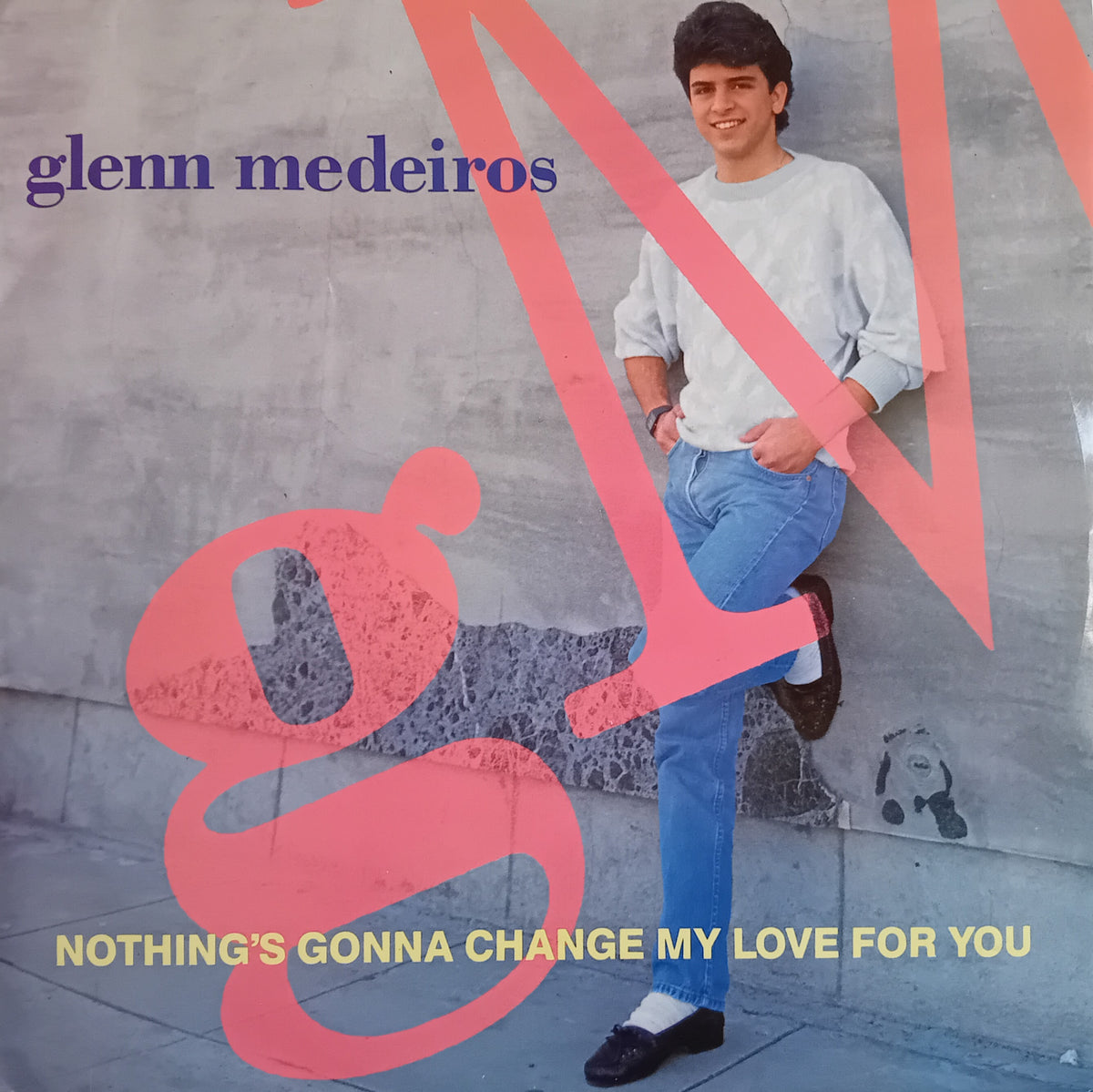 Glenn Medeiros single cover for 'Nothing's Gonna Change My Love For You', featuring a photo of the artist leaning against a concrete wall, overlaid with large pink graphic lettering and purple and yellow text.