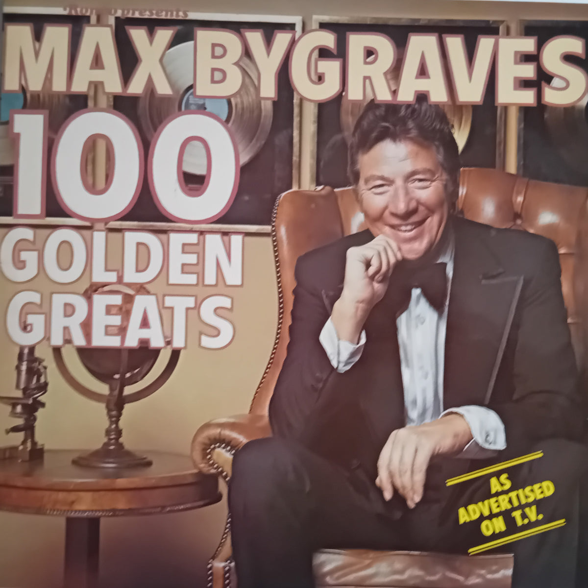 Album cover for Max Bygraves '100 Golden Greats', featuring a portrait of the artist in a black tuxedo sitting in a brown leather armchair, with large white and yellow text on a warm beige background.