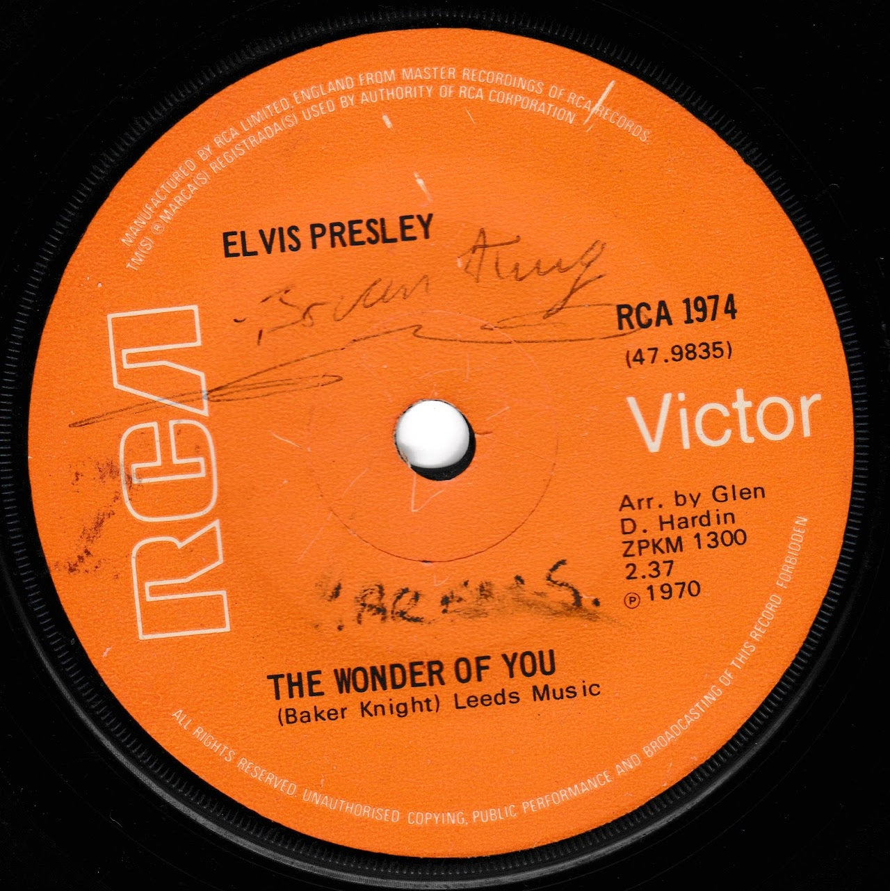 A close-up of a vintage vinyl record label for Elvis Presley's 'The Wonder of You' on RCA Victor. The label is bright orange with white text and logo, featuring pen writing in black ink across the centre.