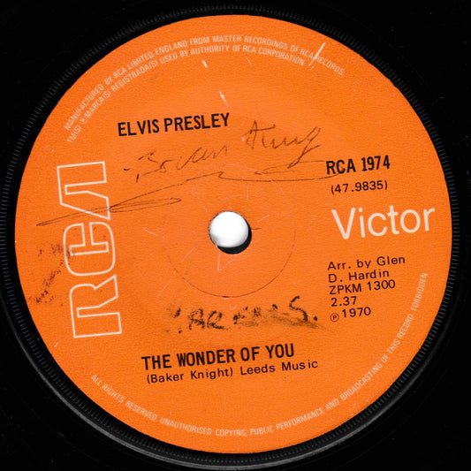 A close-up of a vintage vinyl record label for Elvis Presley's 'The Wonder of You' on RCA Victor. The label is bright orange with white text and logo, featuring pen writing in black ink across the centre.
