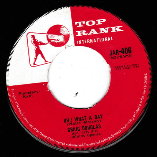 A vintage 7-inch vinyl record label for Top Rank International, featuring the song 'Oh! What a Day' by Craig Douglas with Johnny Spence. The label is red and white with black text and a central white spindle hole, photographed against a black background.