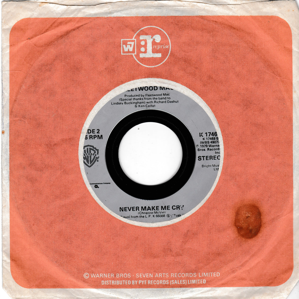 A vintage 7-inch vinyl record sleeve for 'Never Make Me Cry' by Fleetwood Mac, featuring a coral orange cover with a central gray and white label and a small brown spot on the lower right.
