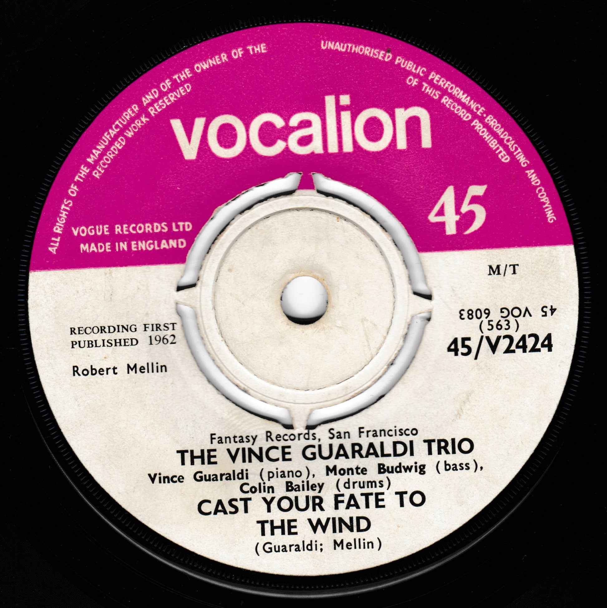 A close-up of a vintage vinyl record label for 'The Vince Guaraldi Trio - Cast Your Fate to the Wind' on Vocalion Records. The label features a magenta-pink outer ring with the brand name in white, and a cream-coloured centre with black text listing the performers and track title.