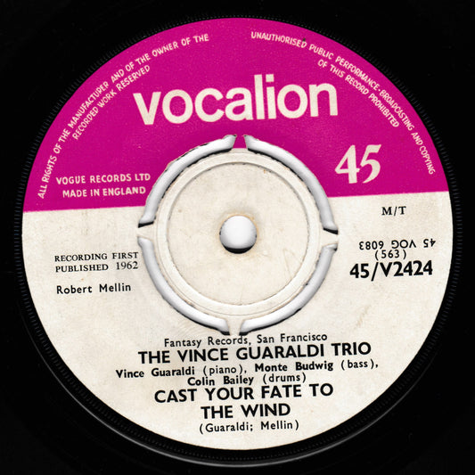 A close-up of a vintage vinyl record label for 'The Vince Guaraldi Trio - Cast Your Fate to the Wind' on Vocalion Records. The label features a magenta-pink outer ring with the brand name in white, and a cream-coloured centre with black text listing the performers and track title.