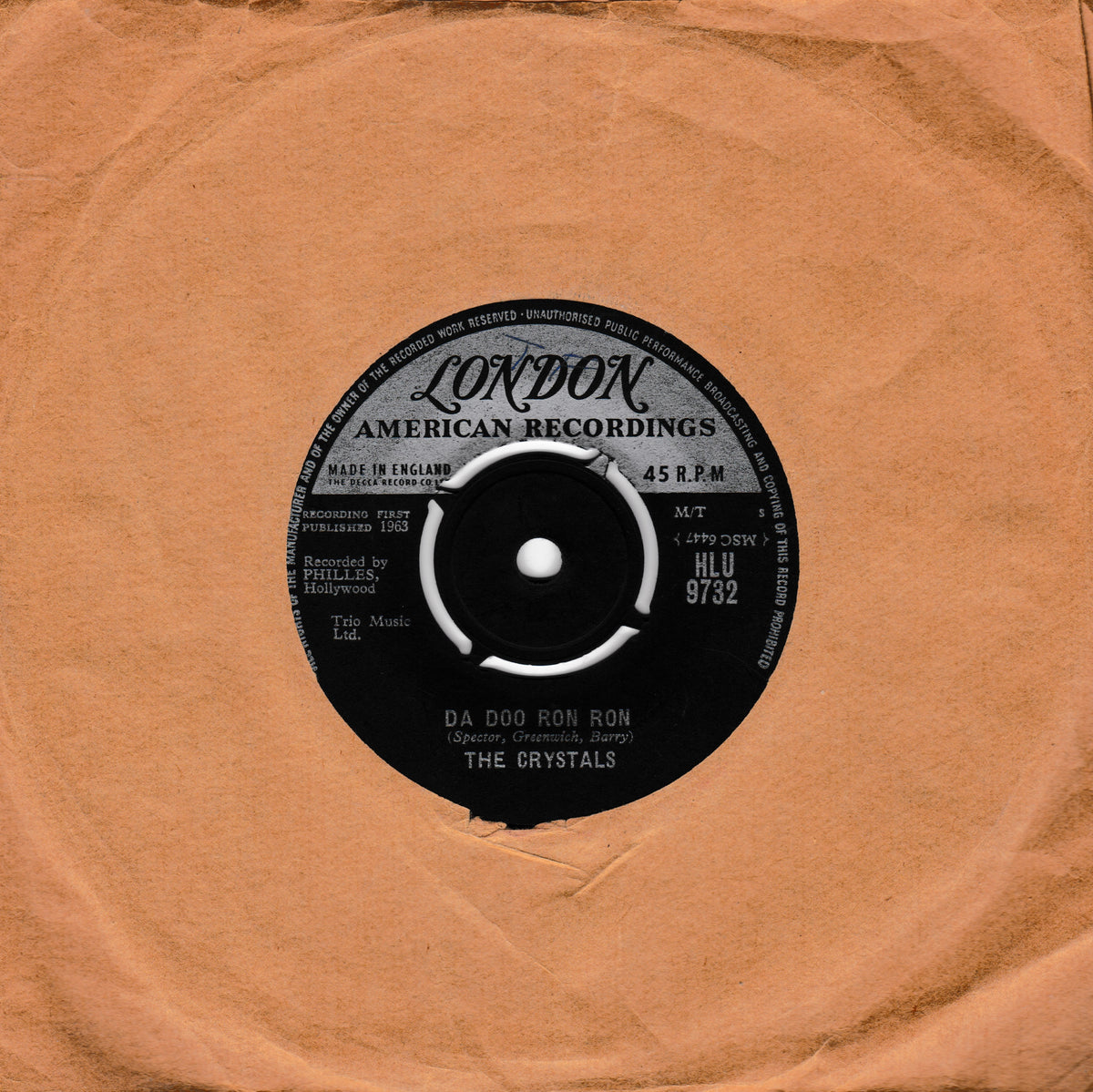A vintage 45 RPM vinyl record from London American Recordings, featuring The Crystals' song 'Da Doo Ron Ron'. The black record label is centered on a square, textured tan paper sleeve.