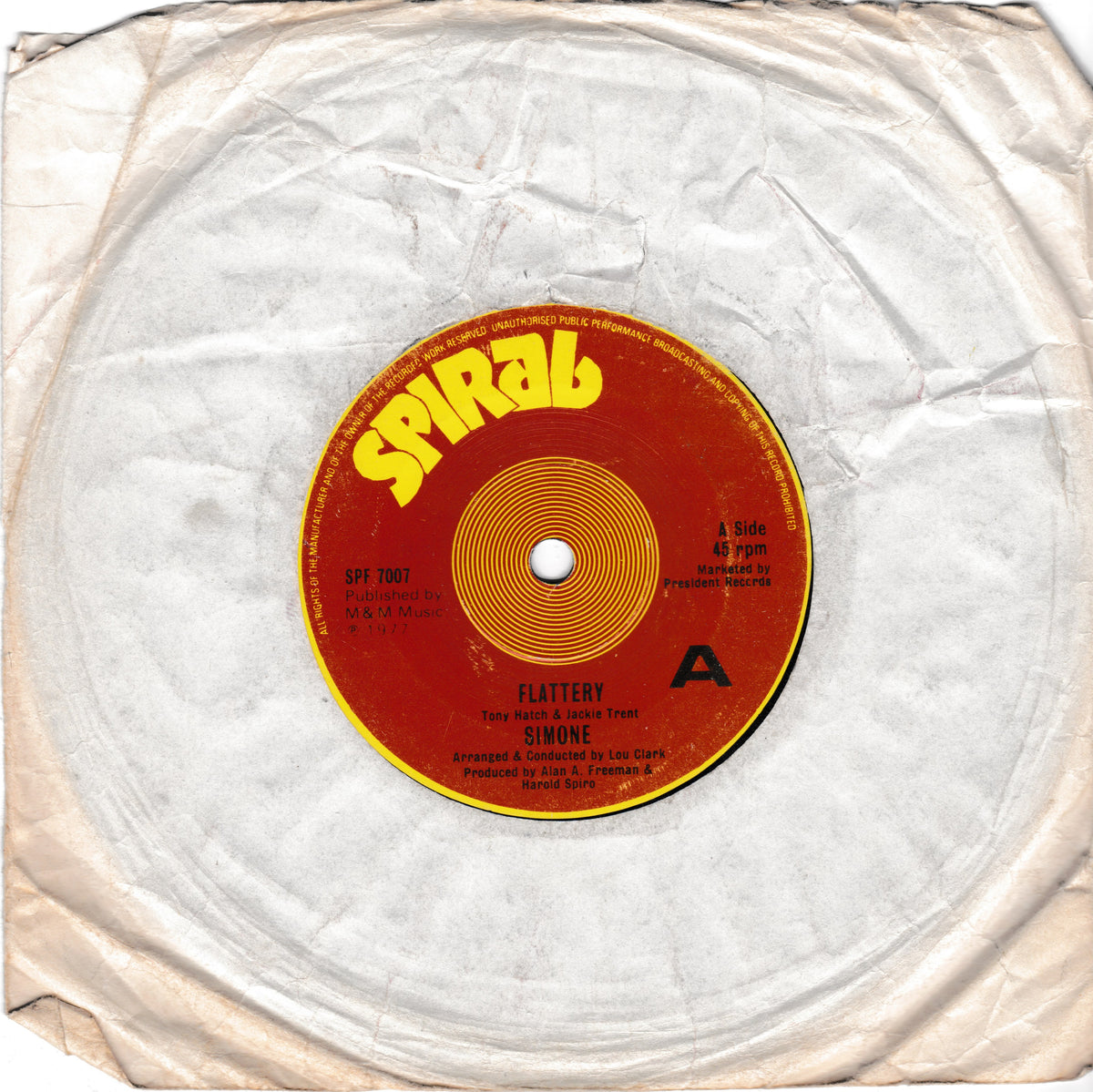A vintage vinyl record partially wrapped in wrinkled white paper, showing the red and yellow Spiral Records label with the song title 'Flattery' and artist 'Simone'.