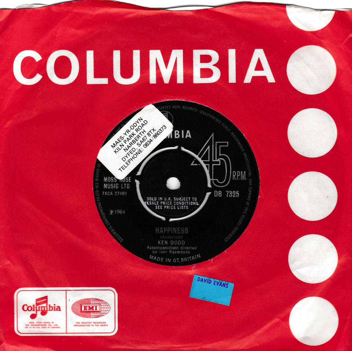 Vintage red Columbia 45 rpm record sleeve with white polka dots, featuring the black centre label for Ken Dodd's 'Happiness'. The sleeve includes a white Columbia logo at the top, a white FMJ Radio sticker at the bottom left, and a blue 'DAVID EVANS' sticker at the bottom right.