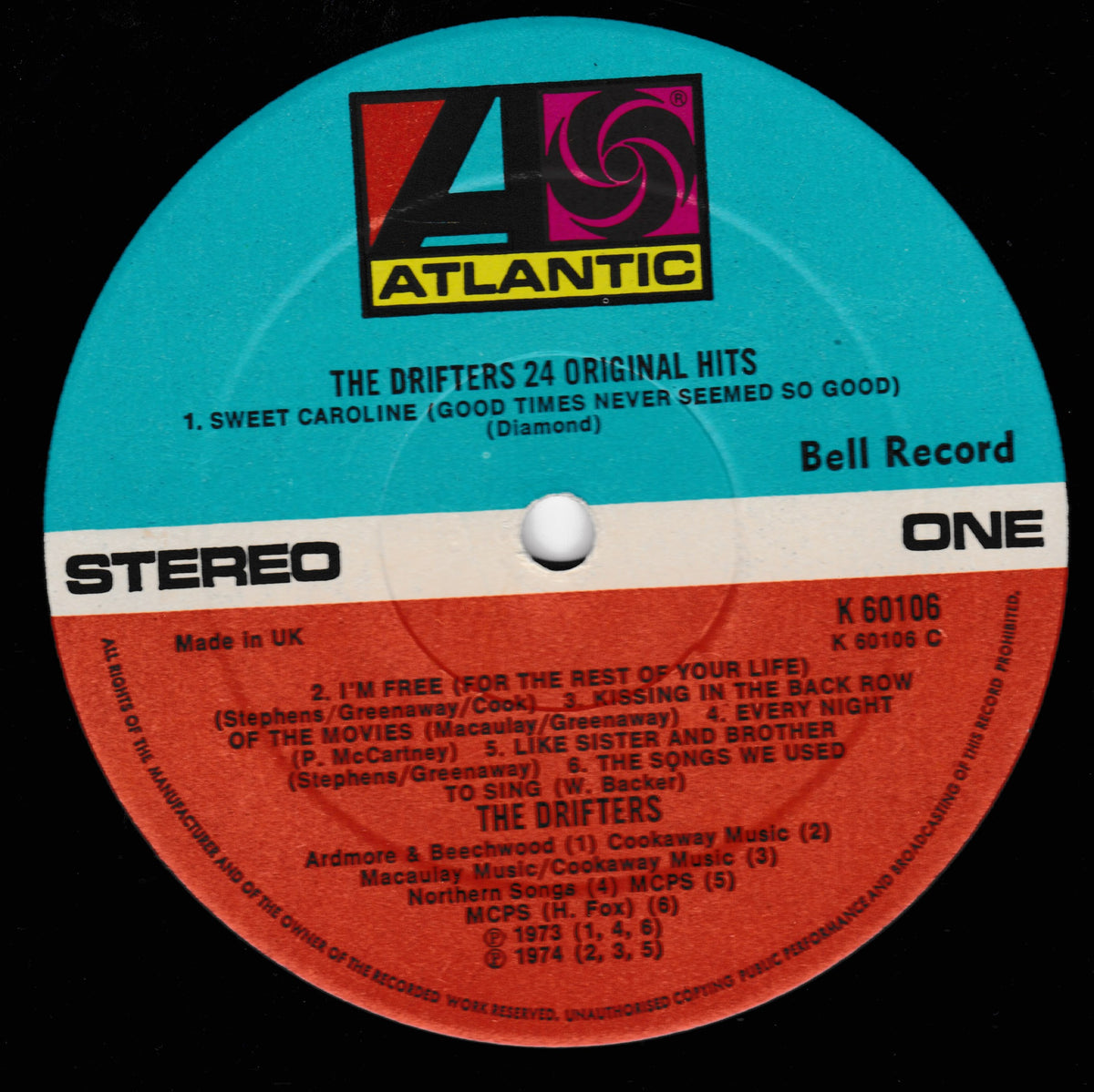 A close-up of a vinyl record label for Atlantic Records' 'The Drifters 24 Original Hits' on Atlantic Records. The label is split horizontally with a turquoise blue top half and a red-orange bottom half, with white text and the Atlantic logo at the top.