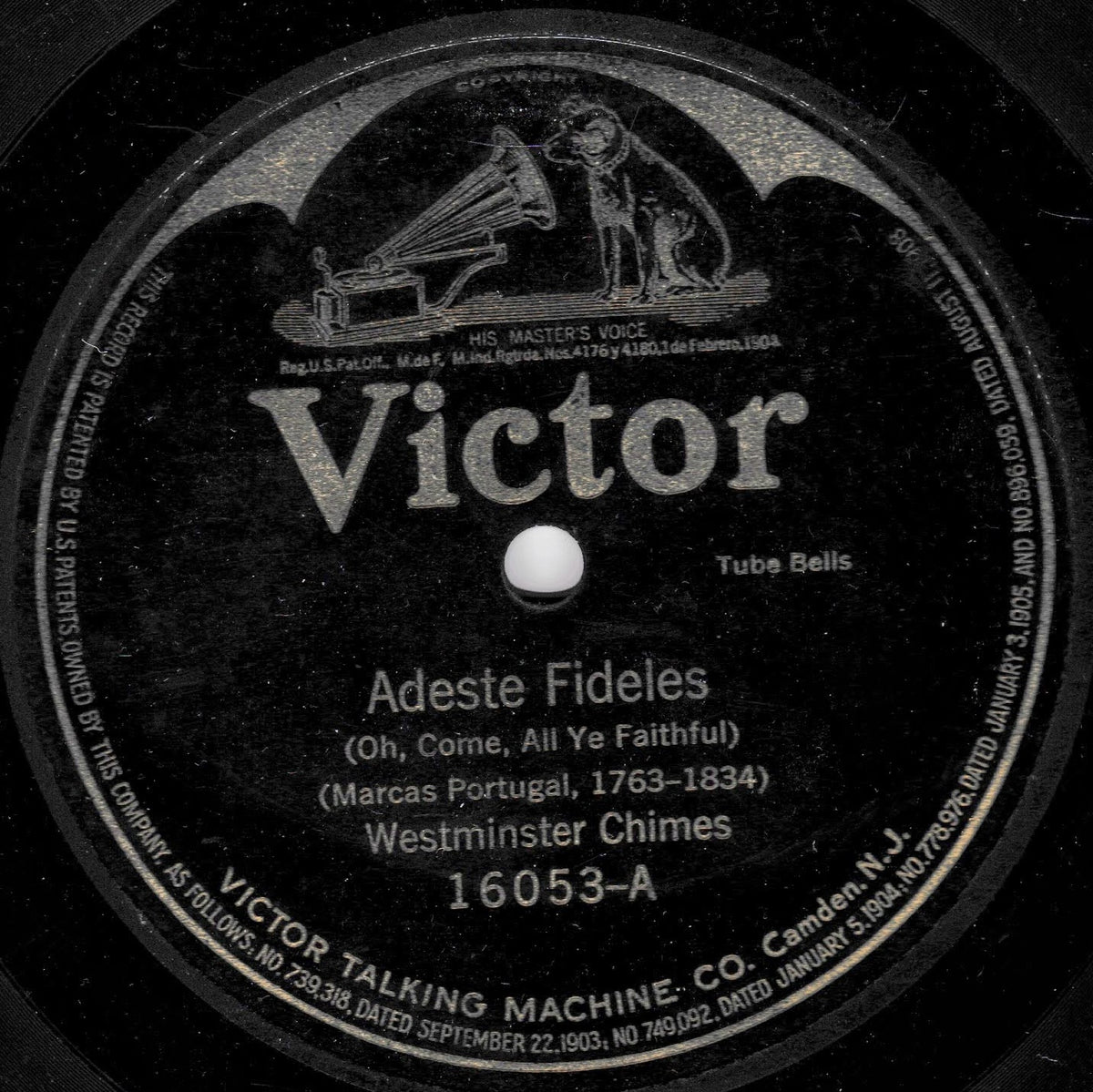 A close-up of a vintage Victor record label reading 'Adeste Fideles' with 'Westminster Chimes' and catalog number '16053-A'. The black circular label has white text and an illustration of a gramophone and dog near the top.