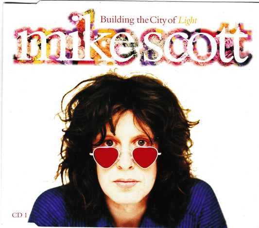 Single cover for Mike Scott's 'Building the City of Light' CD, featuring a portrait of the artist wearing red heart-shaped sunglasses against a white background with colorful stylized text.