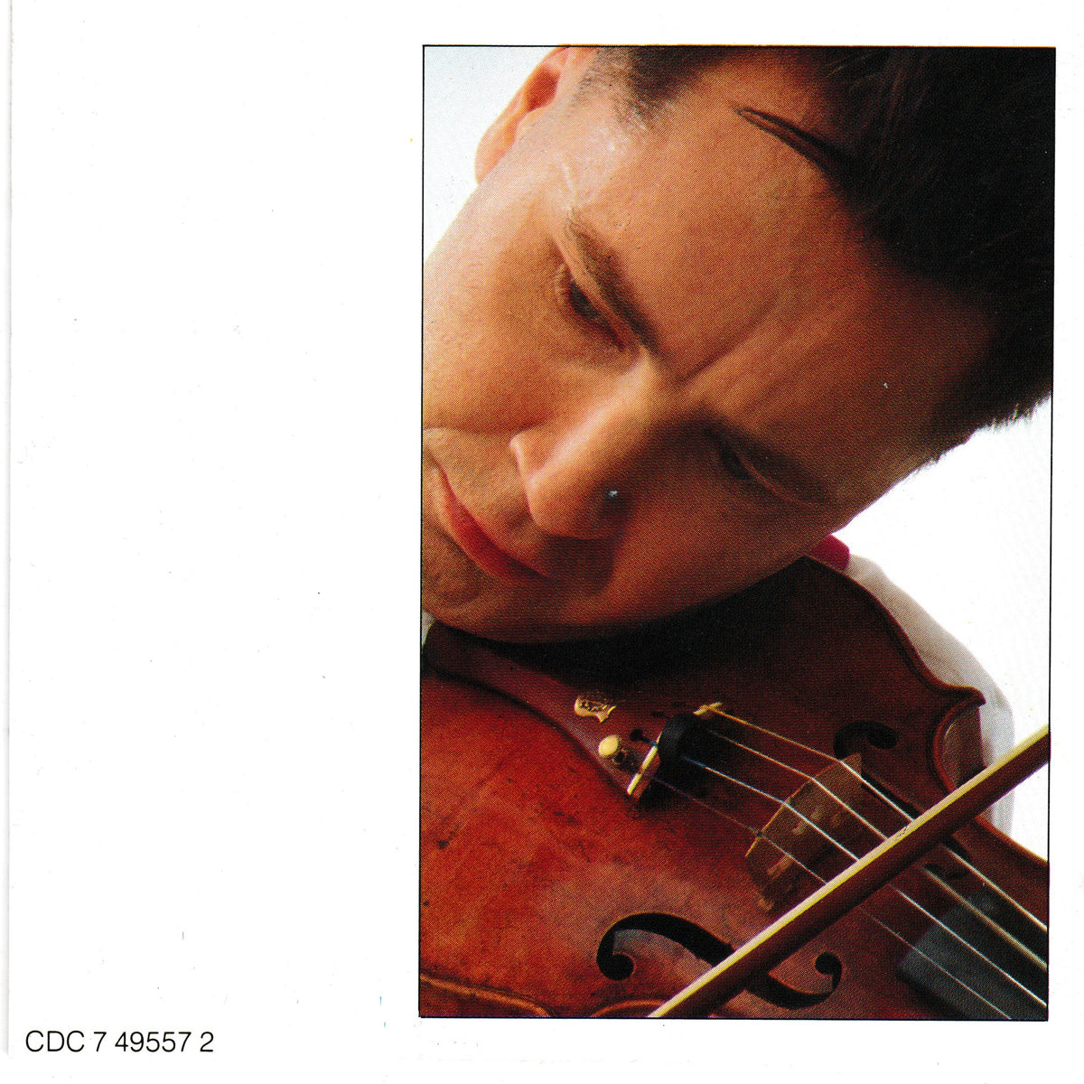 A close-up photograph of a man playing a violin, cropped to show his face, the instrument, and part of the bow against a white background. A narrow black border surrounds the photo, and small text appears in the lower left corner.