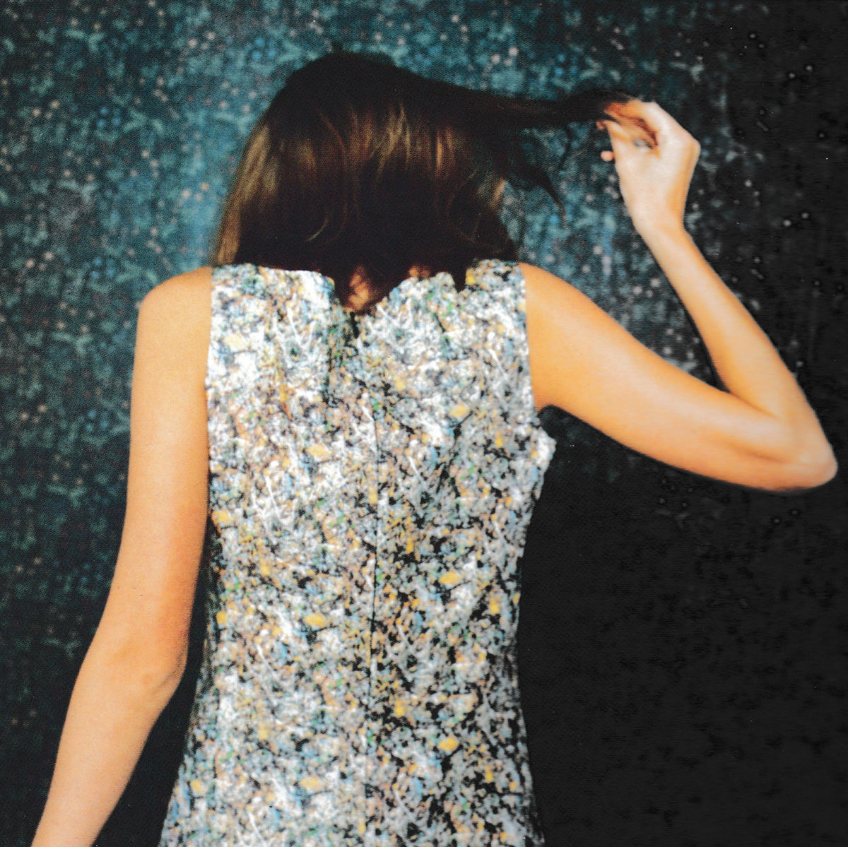 A woman seen from behind wearing a sleeveless dress covered in dense silver, white, and black glitter, with a dark sparkling background.