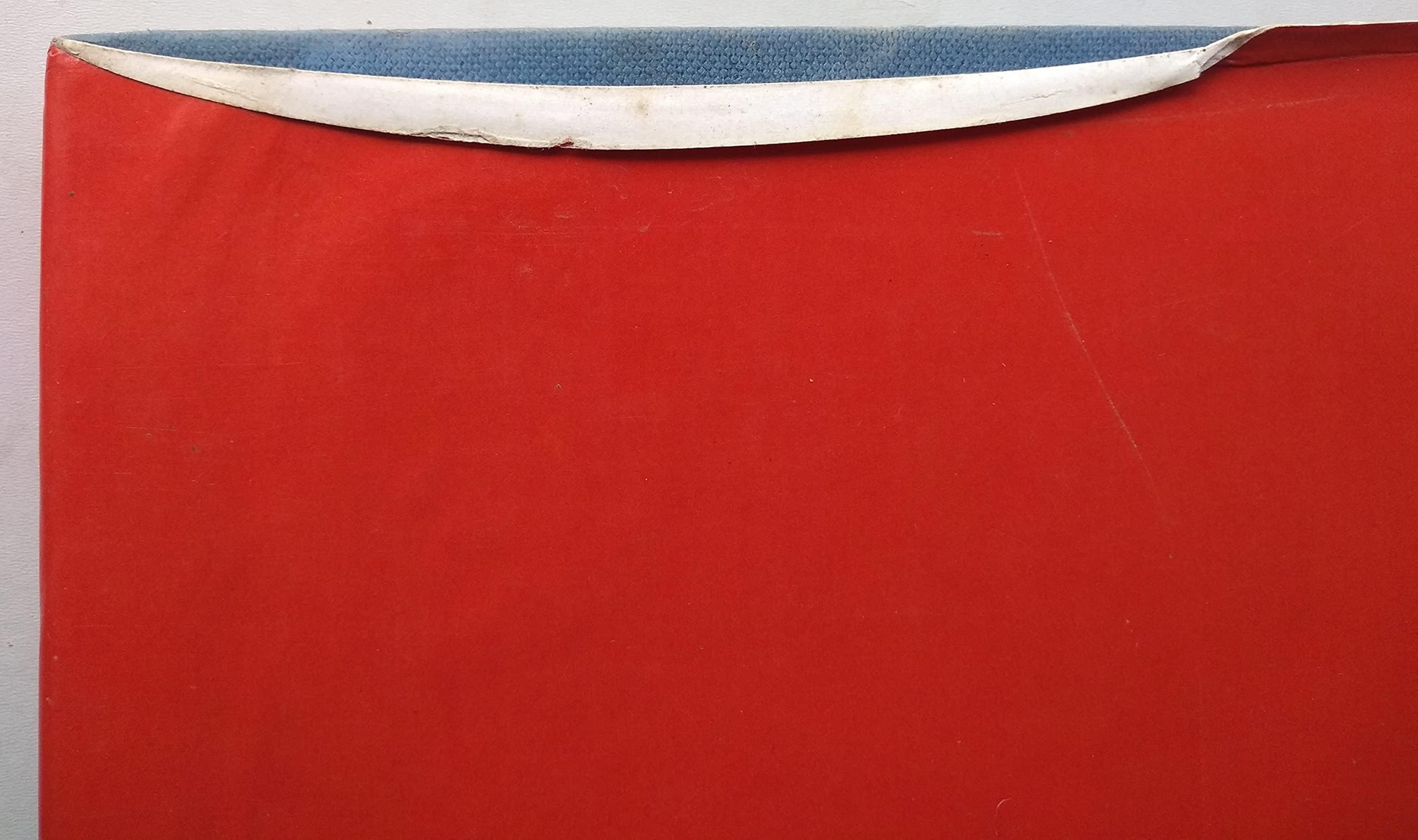 A close-up of a red book dustcover with a white paper edge along the top, photographed against a light background.