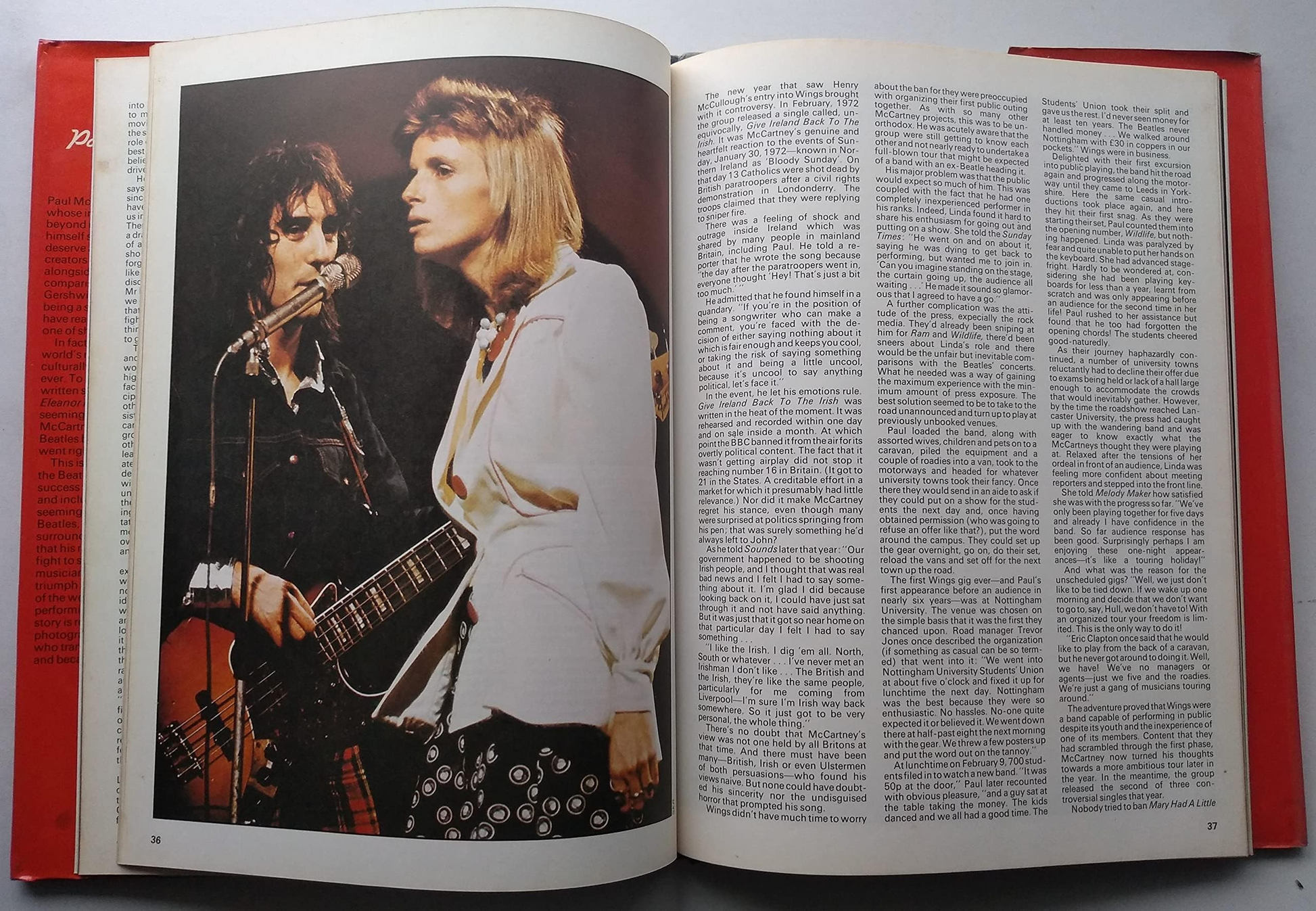 An open book showing a vintage color photograph of a rock band performing on stage on the left page, with dense columns of text on the right page. The book has red side borders.